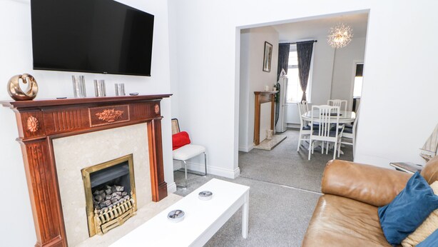 Een woonkamer met een open haard, een aan de muur bevestigde televisie, een witte salontafel en een bruine leren bank.