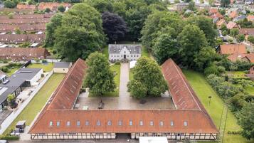 A large, rectangular building with a tiled roof, surrounded by lush greenery and residential buildings.