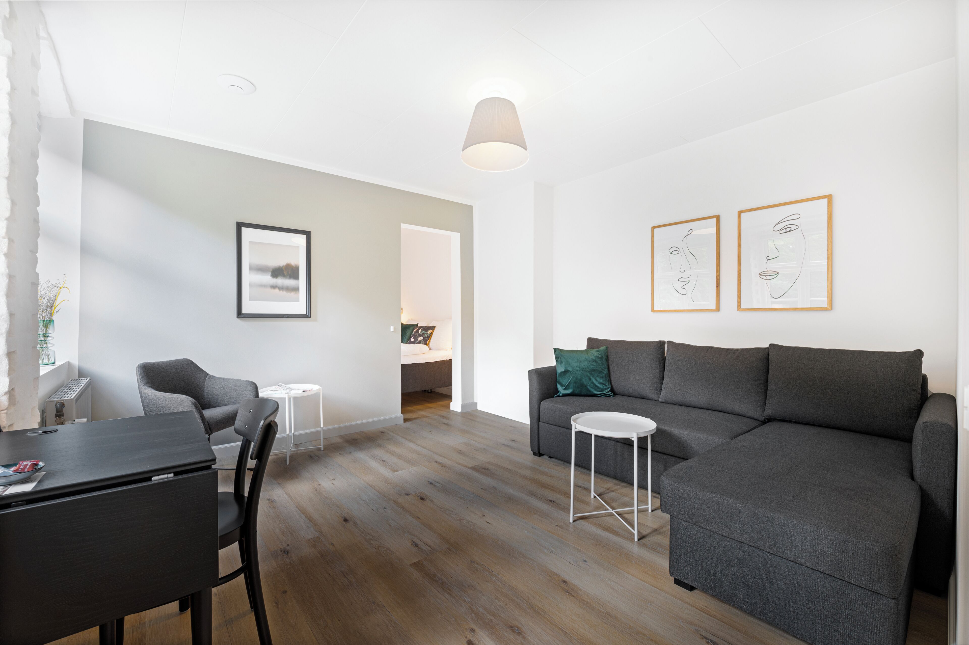 A modern living room with a grey sofa, a small round table, and a dining area with a dark table and chairs.