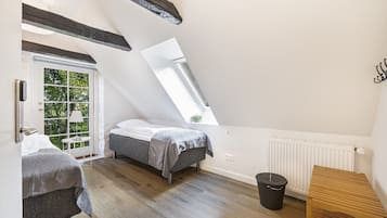 A small, well-lit room with two beds, a window, a radiator, and a wooden bench.