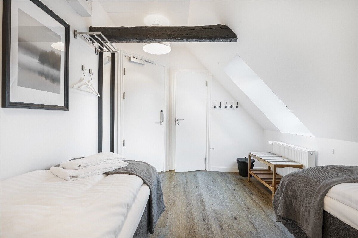 A modern bedroom with a sloped ceiling, a bed, a small table, and a radiator.