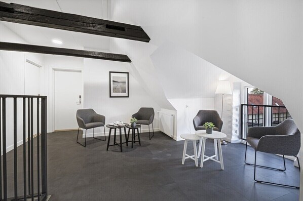 Un loft moderno con vigas a la vista, una escalera y un área de estar con sillas y mesas.