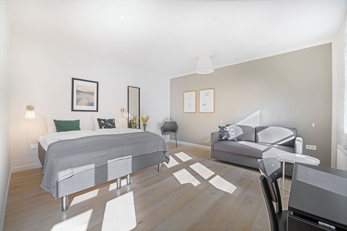 A modern bedroom with a bed, a grey sofa, a small table, and a chair.