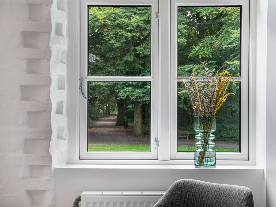 Una ventana con vistas a un parque, un florero con flores y un radiador debajo.
