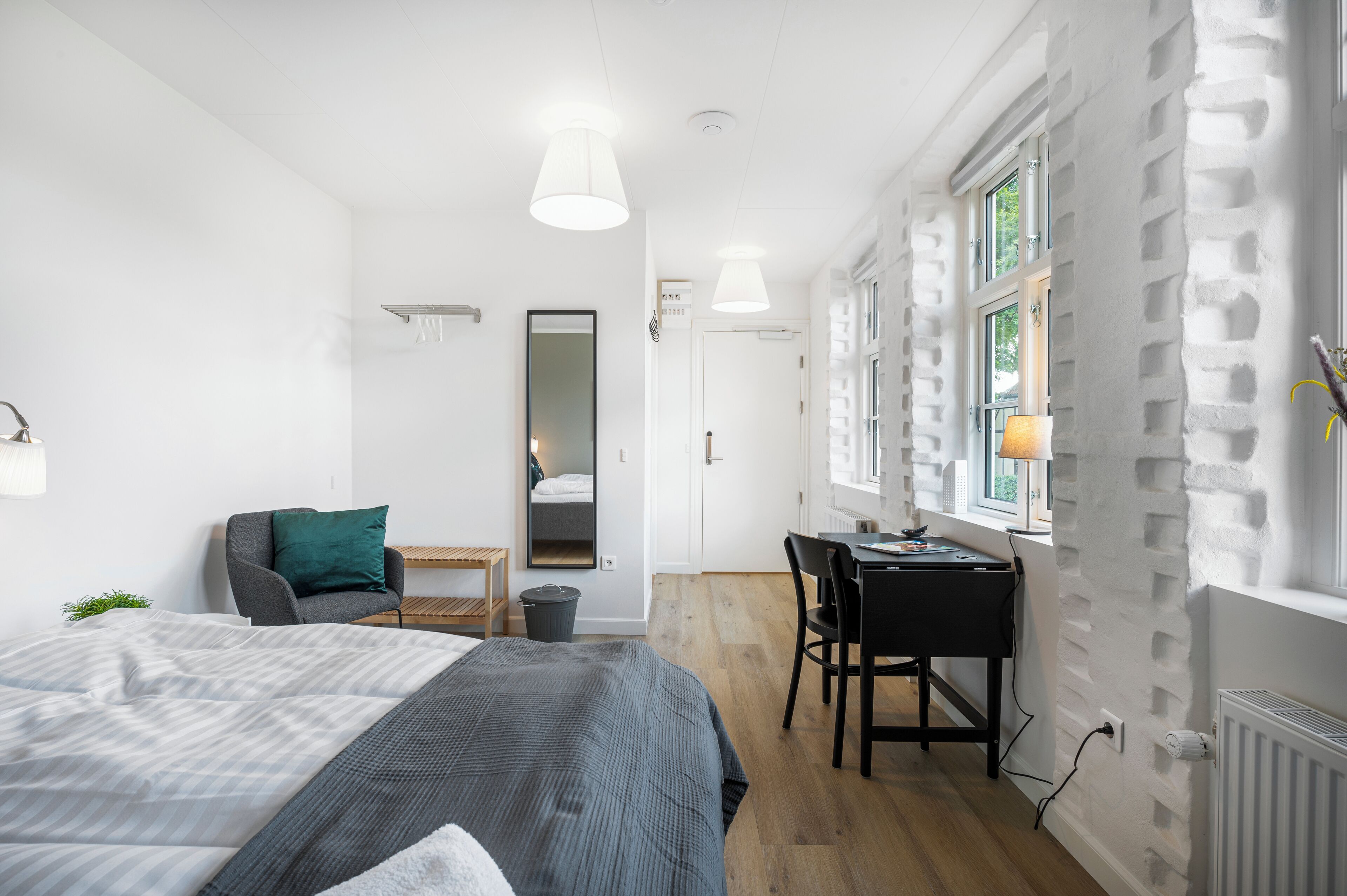 A modern bedroom with a bed, desk, and chair, a mirror, and a window with a view.