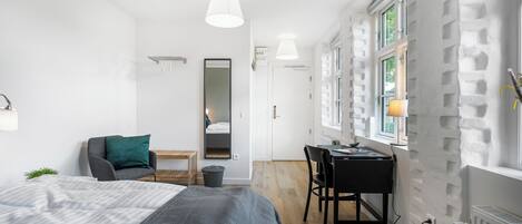 A modern bedroom with a bed, desk, and chair, a mirror, and a window with a view.