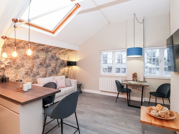 Une cuisine moderne avec un plan de travail en bois, un coin repas avec une table et des chaises, et un espace de vie avec un canapé et un téléviseur.
