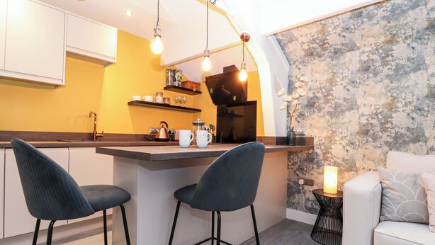 A modern kitchen with a central island, two bar stools, a white sofa, and a textured wall. - Fenty's (Windermere)
