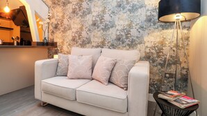 A modern living room with a textured wall, a sofa with decorative pillows, a floor lamp, and a small side table with magazines. - Fenty's (Windermere)