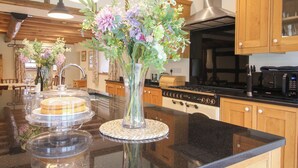 Une cuisine avec des armoires en bois, une hotte de cuisinière en acier inoxydable, un four à micro-ondes et un grand îlot central agrémenté d’un vase de fleurs.