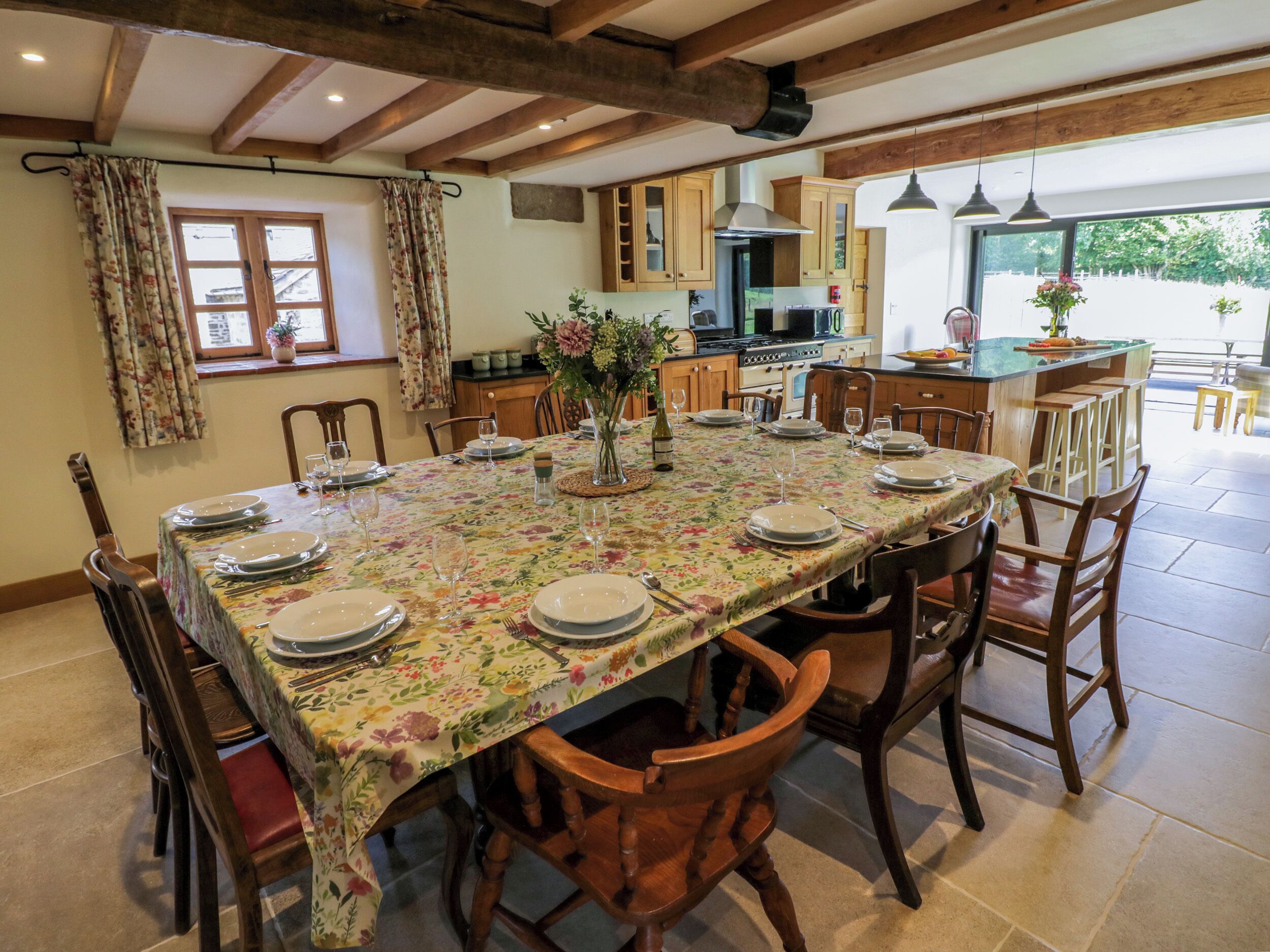 Zona pranzo con un lungo tavolo apparecchiato per sei persone, sedie di legno e una cucina sullo sfondo.