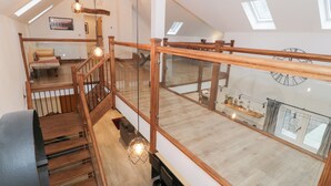 A spacious loft with a wooden staircase, a cozy seating area, and a view of the city through large windows. - Merddwr (Corwen)