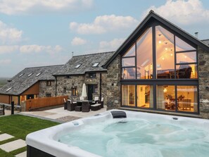 A modern house with a stone exterior, a large glass conservatory, and a hot tub in the foreground. - Merddwr (Corwen)