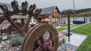 A rustic metal sculpture in a garden area with a stone house in the background. - Merddwr (Corwen)