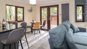 A dining area with a table set for four, a sofa, and a view of the outdoors. - Alfresco Lodge (Windermere)