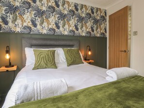 Una cama bien hecha con ropa de cama verde y blanca, dos lámparas de noche y un cabecero estampado con motivos florales.