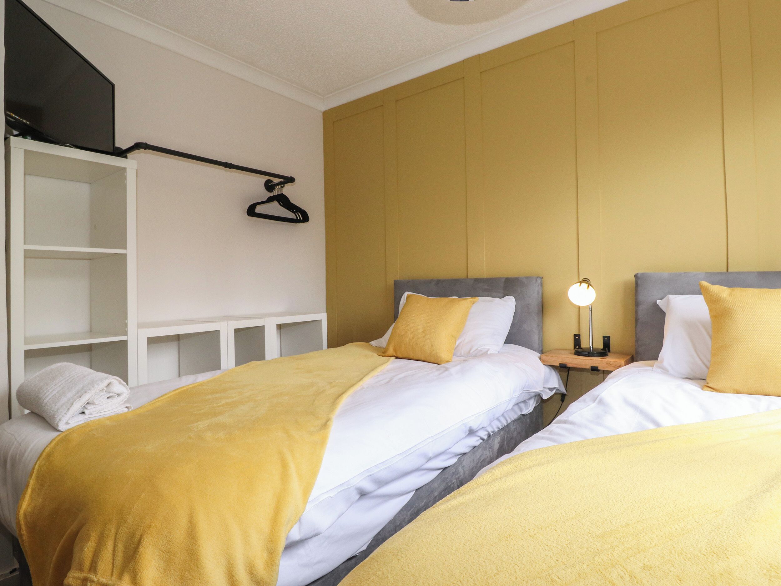 A hotel room with two beds, a wardrobe, and a bedside table with a lamp.
