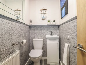 Un baño pequeño y funcional con inodoro, lavamanos y un estante con plantas.