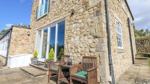 A stone building with a large glass door, wooden furniture, and a small outdoor seating area.