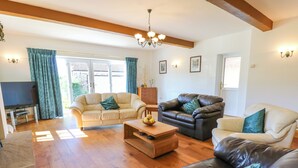 A spacious living room with a wooden floor, leather sofas, a coffee table, and a TV.