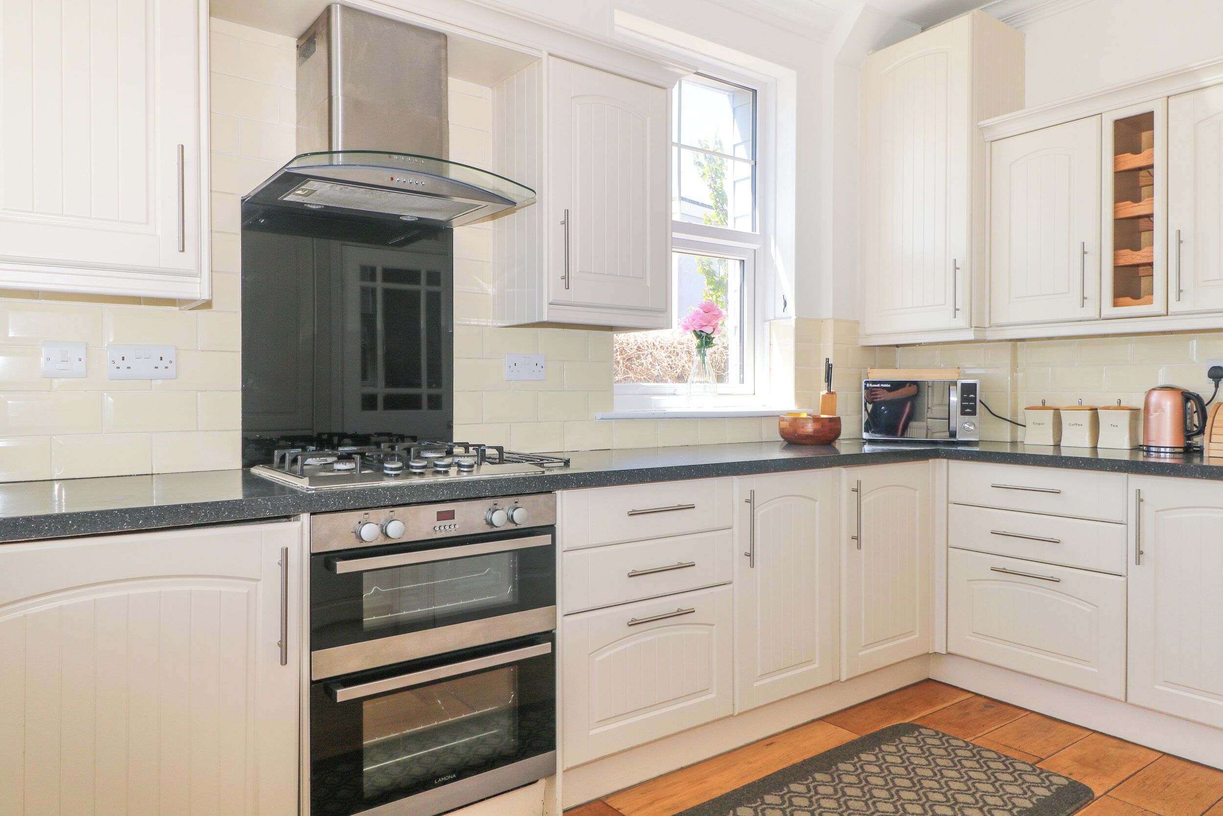 A kitchen with white cabinets, a gas stove, an oven, and a window with a flower vase.