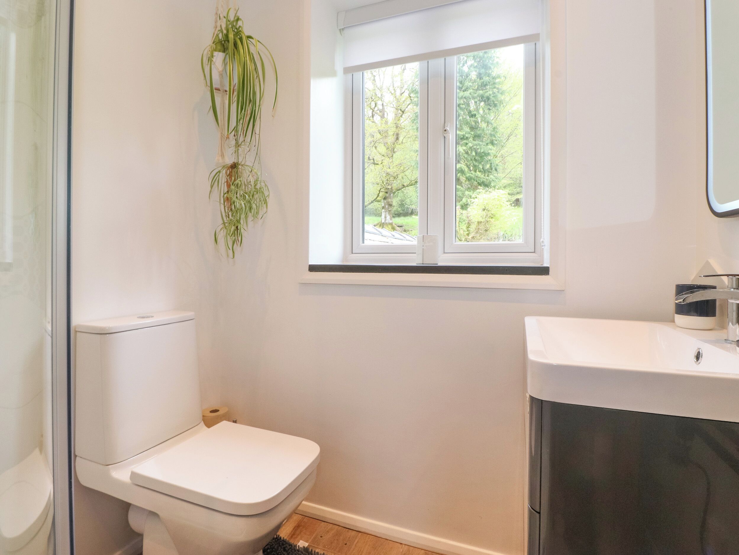 A small, modern bathroom with a toilet, a window with a view of greenery, and a sink with a mirror.