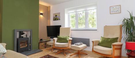 A living room with two armchairs, a sofa, a fireplace, a television, and a window with a view of greenery.