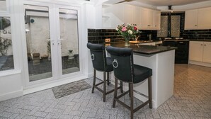 Une cuisine moderne dotée d’un grand îlot central, de deux tabourets de bar et d’une porte vitrée donnant sur un espace extérieur.
