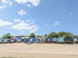 Una hilera de cabañas de playa con pasarelas de madera que las conectan, ubicadas en una playa arenosa bajo un cielo despejado.