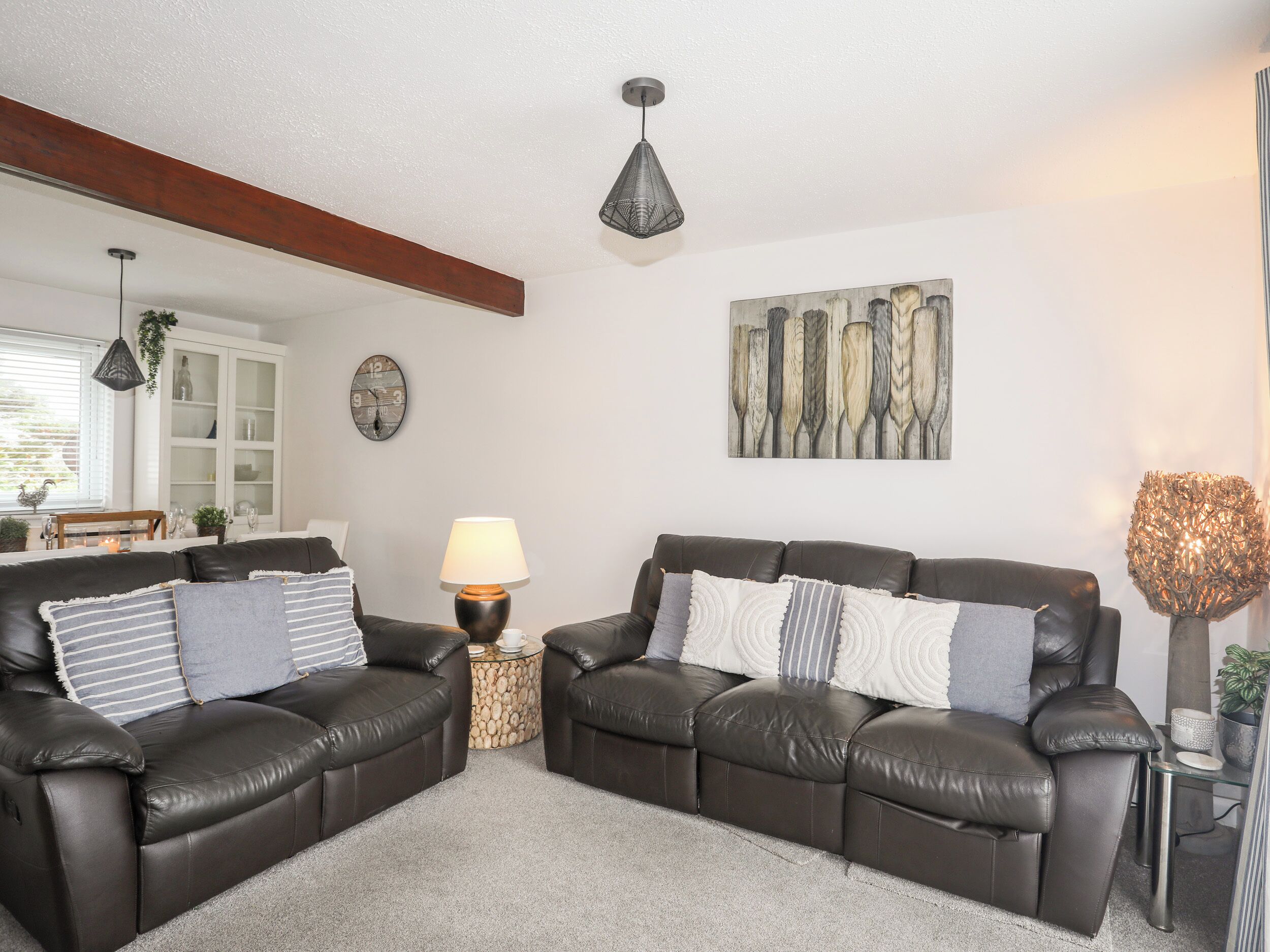 A living room with two dark leather sofas, a round coffee table, a lamp, a clock, and a painting on the wall.
