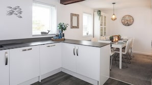 Una cocina moderna con armarios blancos, una encimera negra y un comedor con mesa y sillas blancas.