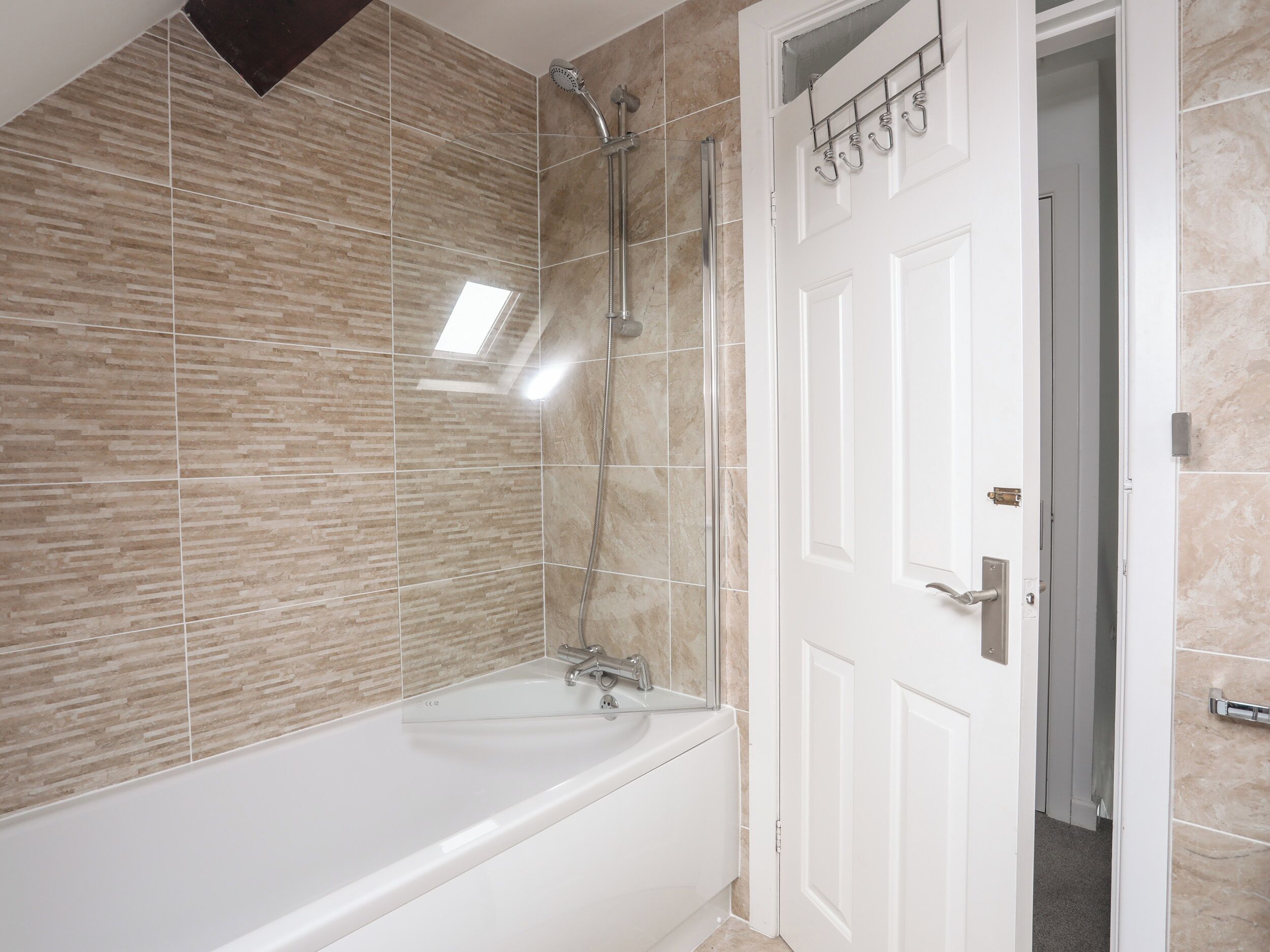 A bathroom with a bathtub, shower, and a door leading to another room.