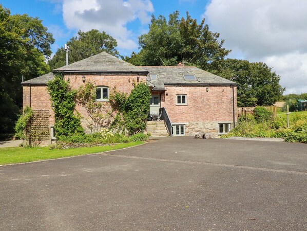 A two-story brick house with a sloped roof, a front entrance with steps, and a driveway leading to the front door. - The Old Watermill (Bodmin)