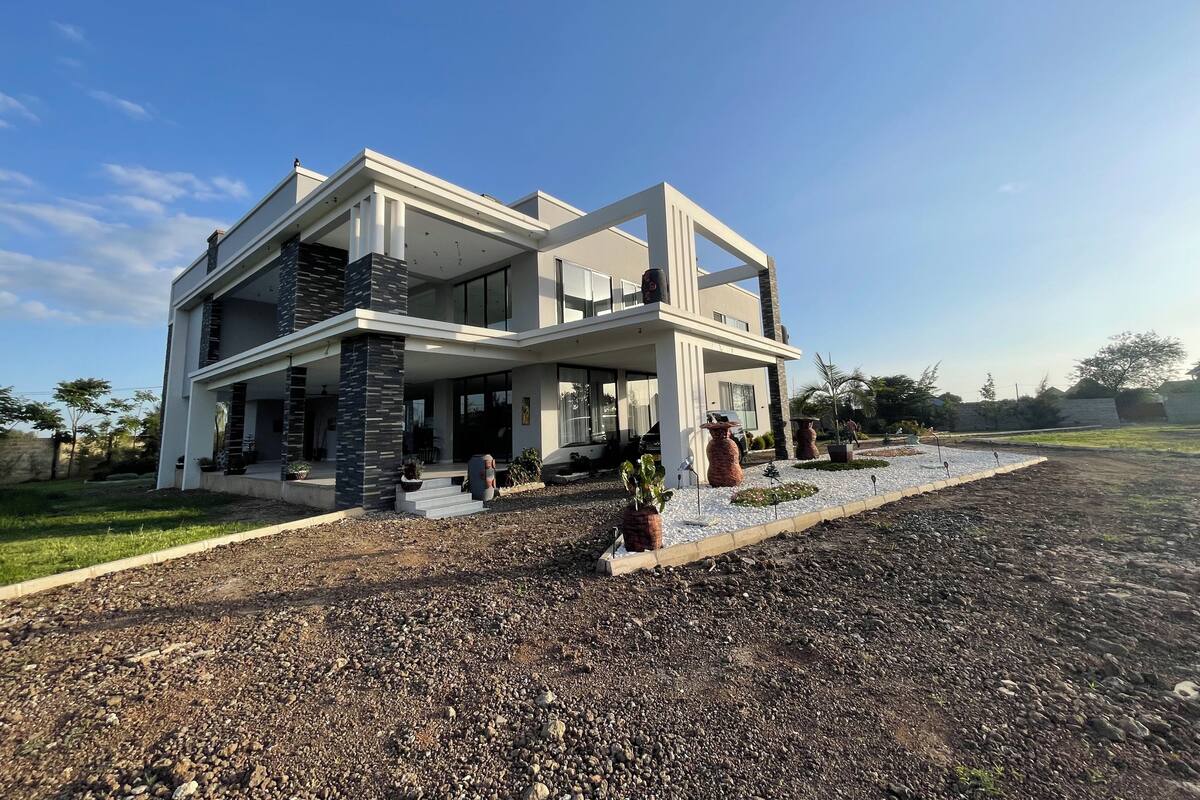 Une maison moderne à deux étages, dotée d’un vaste porche à l’avant, de grandes fenêtres et d’un jardin bien entretenu.