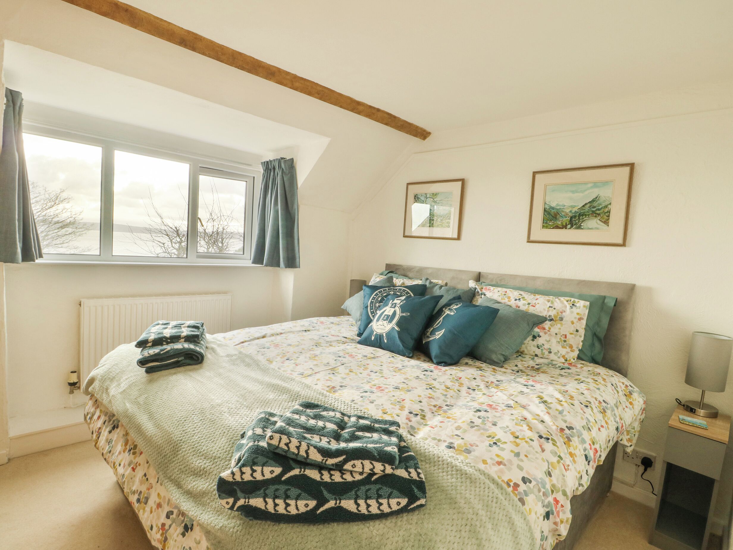 Een slaapkamer met een bed, een raam, een radiator, een lamp en twee ingelijste foto’s aan de muur.
