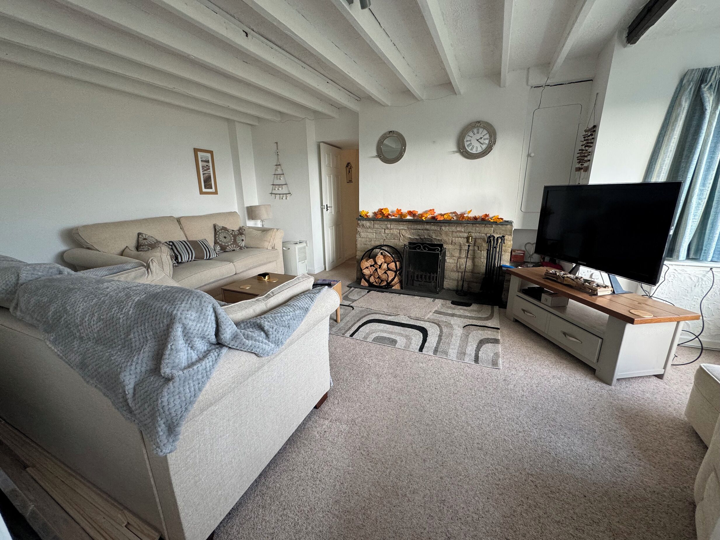 A living room with a sofa, a television, a fireplace, and a clock on the wall.