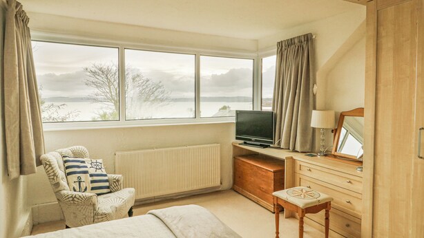 A bedroom with a bed, a chair, a TV, a dresser, and a window with a view of the outdoors. - Bryn Teg Cottage (Moelfre)