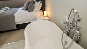 Ein modernes Schlafzimmer mit einer großen Badewanne, einem ordentlich bezogenen Bett und einem Oberlicht.