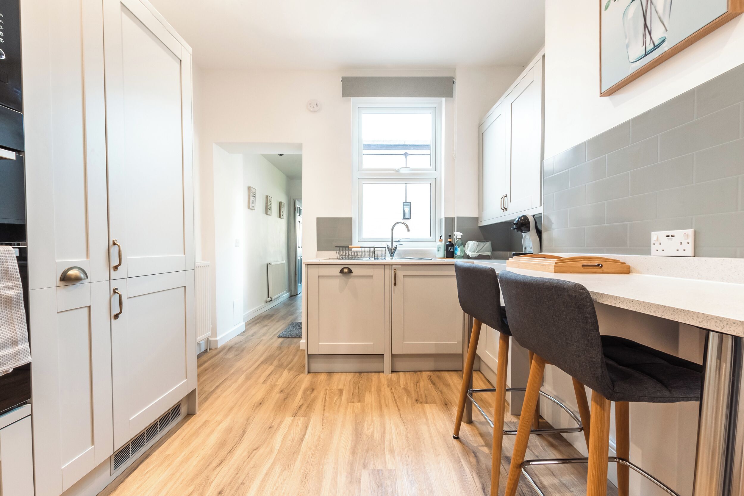 A modern kitchen with white cabinets, a wooden floor, and a bar area with stools.