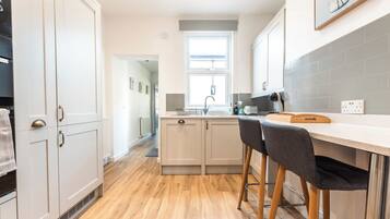 A modern kitchen with white cabinets, a wooden floor, and a bar area with stools.