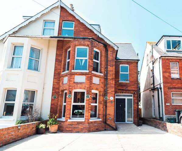 A corner house with a brick facade, white upper floor, and a black door. - Anchor House (Weymouth)