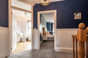 A hallway leading to a bedroom with a bed, a nightstand, and a mirror on the wall. - Anchor House (Weymouth)