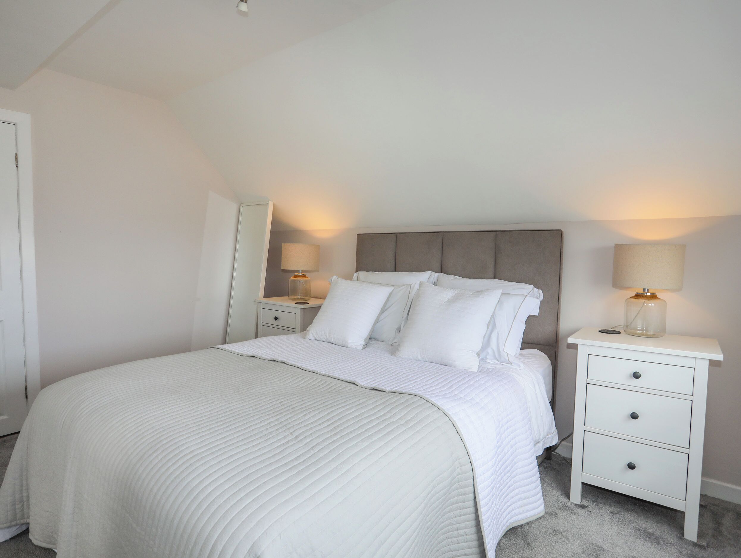 A bedroom with a bed, nightstands, and a mirror.
