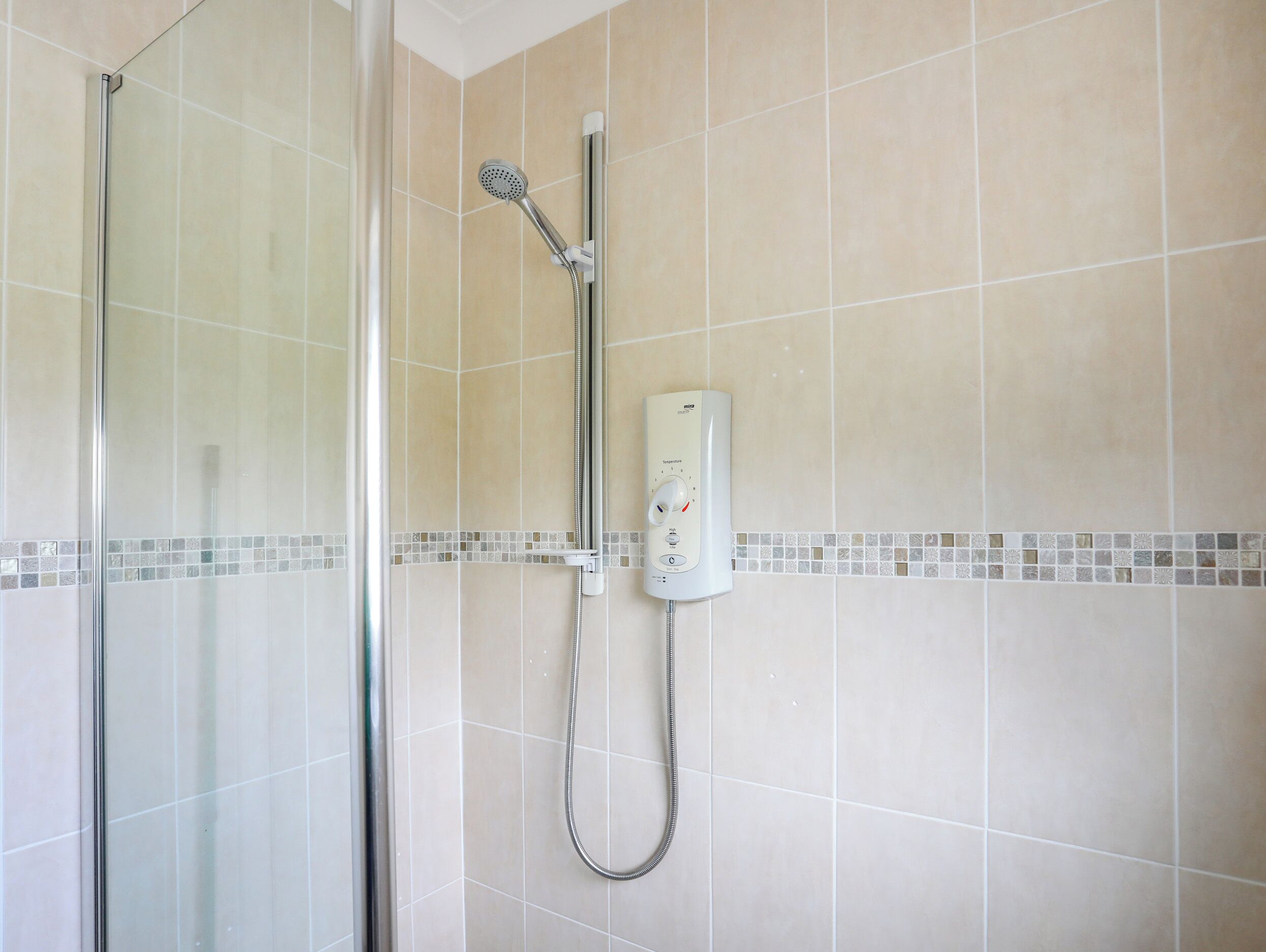 A shower with a handheld showerhead and a wall-mounted control panel.