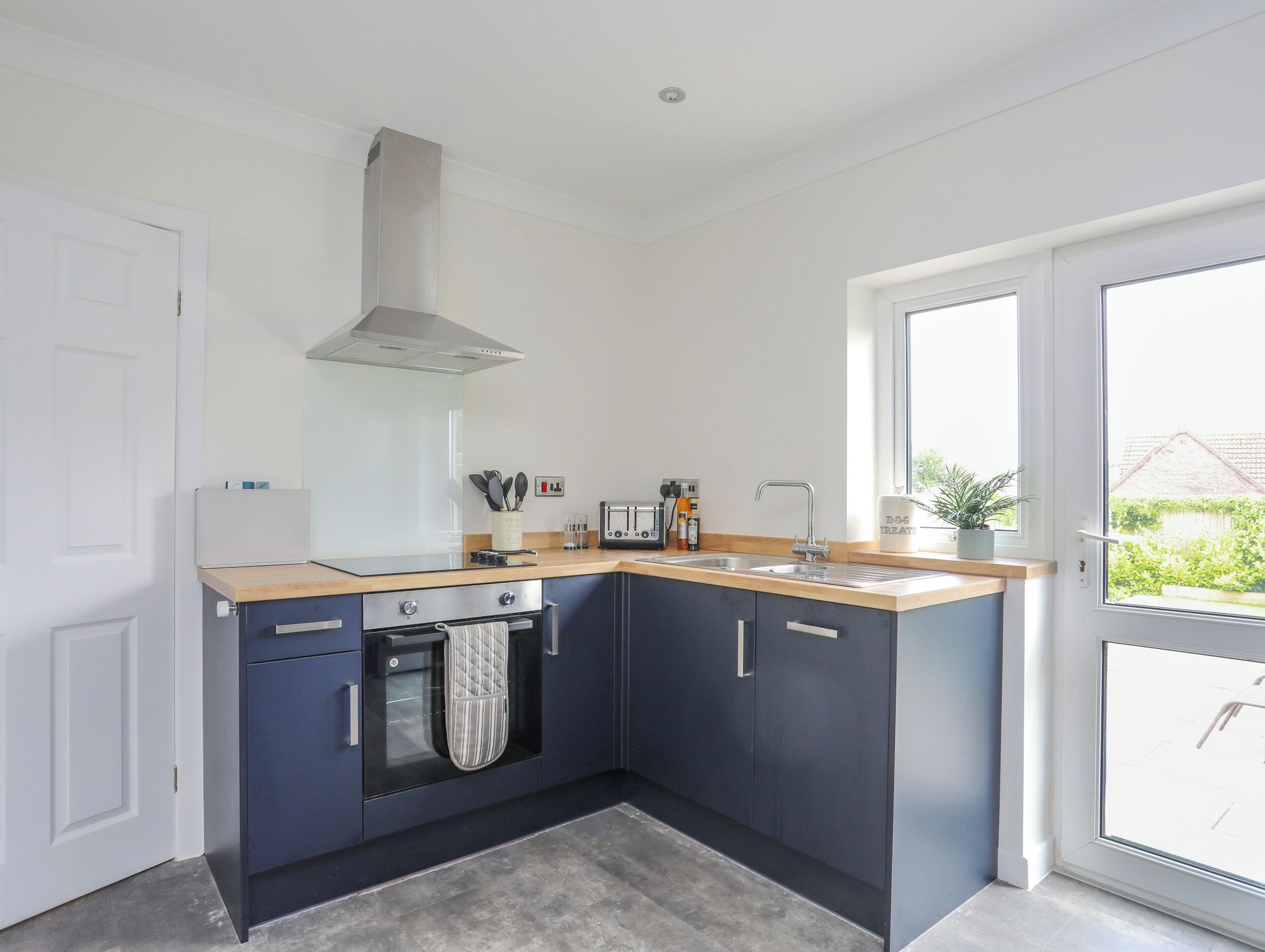Una cocina moderna con armarios azul oscuro, una campana extractora de acero inoxidable, un lavamanos doble y un ventanal que proporciona luz natural.