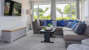 A living room with a sofa set, a floor lamp, a coffee table, and a TV mounted on the wall. - Swn Y Mor (Tyn-y-Gongl)