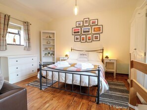 A bedroom with a bed, a dresser, a nightstand, a shelf with decorative items, and a wall with framed pictures. - Woodstock Lodge (Cannock)