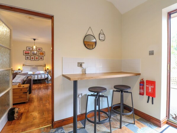A compact kitchen with a wooden countertop, two stools, a mirror, and a fire extinguisher. - Woodstock Lodge (Cannock)