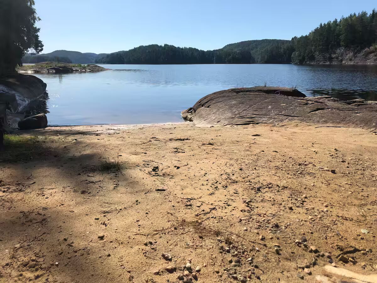 Une plage de sable avec un grand rocher au premier plan et un lac paisible en arrière-plan.