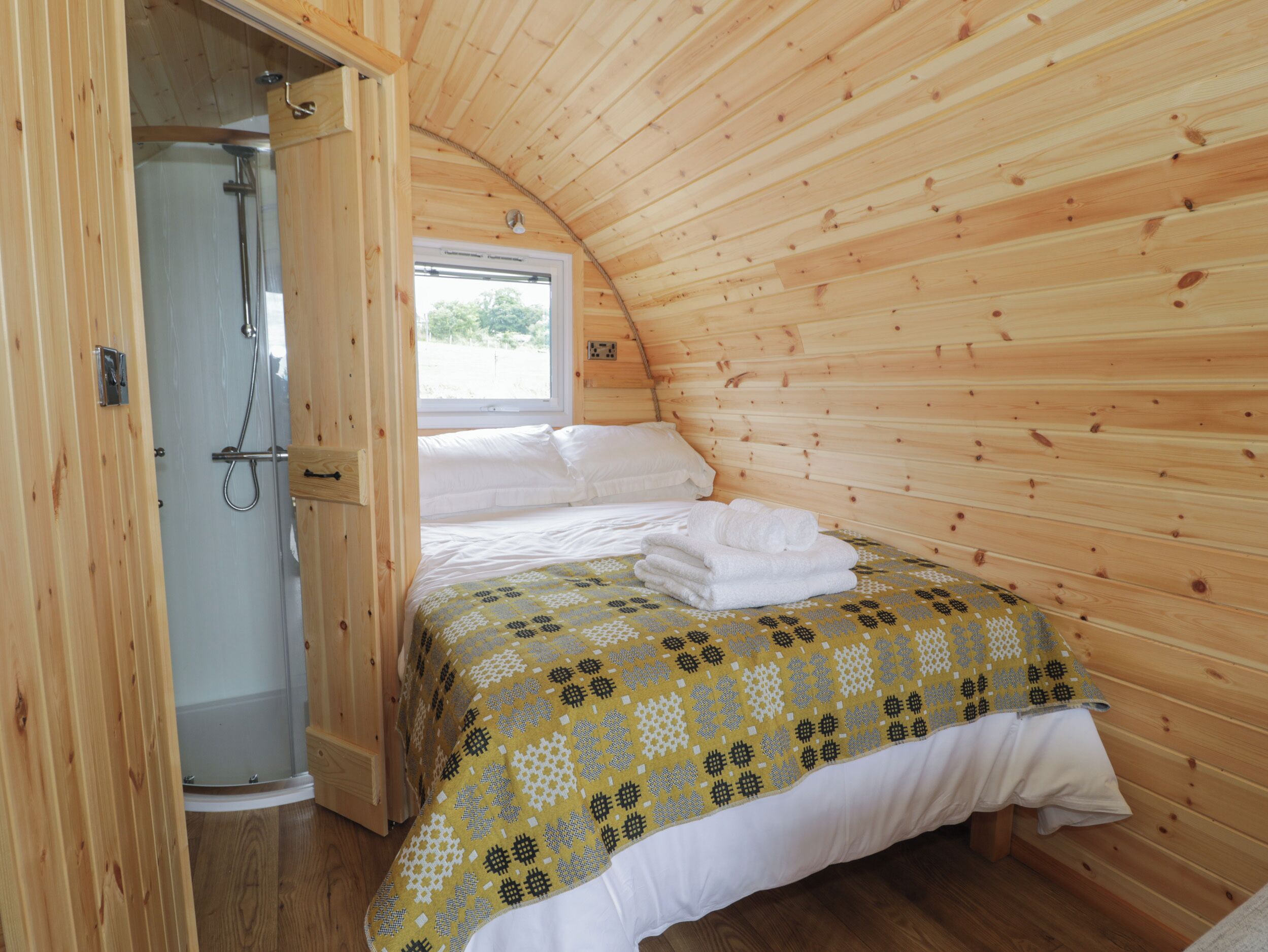 A wooden cabin bedroom with a bed, a shower, and a window.